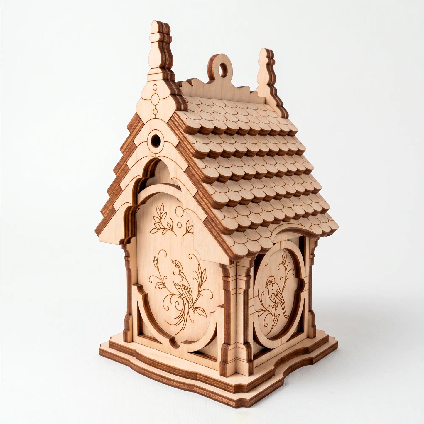 An unpainted natural laser-cut plywood birdhouse showing intricate floral and bird engravings on its side walls and roof.