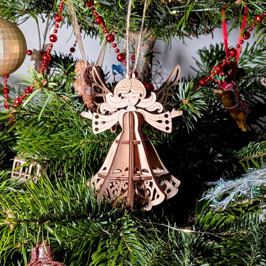 3D laser cut plywood angel ornament hanging by twine string among lush green pine needles and festive red garland beads.