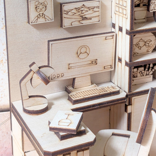 Close-up of a miniature wooden desk and chair in a dollhouse bedroom book nook, showing laser cut details of a computer, lamp, books and shelves. Digital laser cutting file for SVG DXF AI CDR