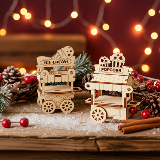 A pair of detailed laser cut wooden plywood miniature street carts—one for "ICE CREAM" and one for "POPCORN"—set on a wooden surface dusted with faux snow, surrounded by pine cones and red berries, with warm string lights in the background.