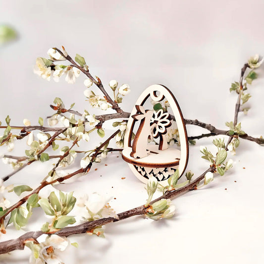 Laser cut plywood wooden Easter egg ornament with a detailed cutout of a bunny holding a flower, framed by white blooming spring tree branches on a white background