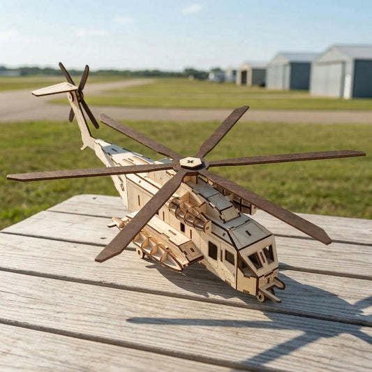 A 3D laser cut plywood helicopter model on a wooden picnic table. 3/4 view shows detailed cockpit windows, side pods, and a large 6-blade rotor. Natural wood finish with dark burnt edges. Background shows a grassy airfield and hangars.