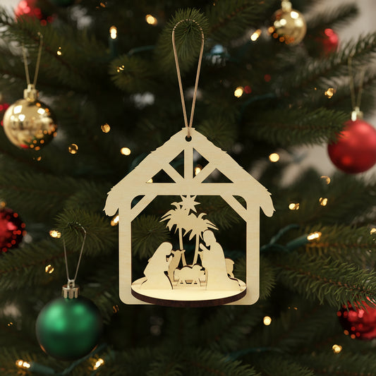 Delicate laser cut Nativity scene featuring a detailed Holy Family manger scene framed in a rustic stable shape with hanging loop, set against a festive lighted Christmas tree background.