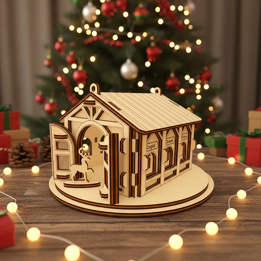Intricate laser cut reindeer barn ornament featuring Santa's stable with arched entry, visible reindeer silhouette, and named stalls, set against a warm fairy lights and gift-wrapped background.