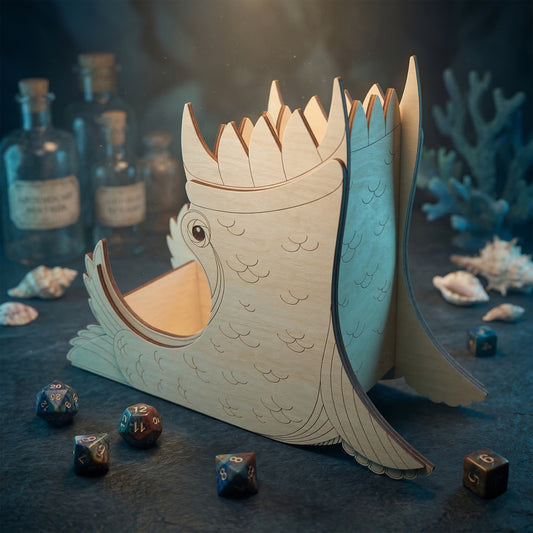 A sea monster dice tower made of laser cut plywood with etched scales and fins. The creature-shaped tower has a jagged top and a tray where polyhedral dice land. Displayed on a dark surface with shells and glass bottles.