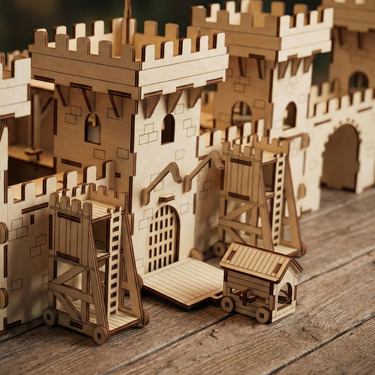 Perspective view of laser cut plywood castle walls with two siege towers and a battering ram positioned at the gate. The image emphasizes the scale and realistic medieval design of the wooden assembly kit.