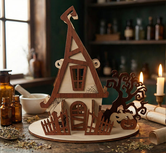 Front view of a spooky laser cut plywood dollhouse. The dark wood frame highlights a boarded-up door and spiderweb engravings. To the right, a silhouette of a gnarled dead tree and two carved pumpkins add a Halloween atmosphere.