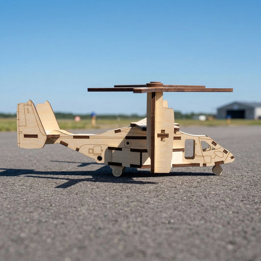 Side profile of a laser cut plywood tiltrotor model. Showcases the wooden fuselage, tail fins, and landing gear wheels. The large rotors are tilted upward in helicopter mode. Clear blue sky and a blurred hangar are visible in the distance.