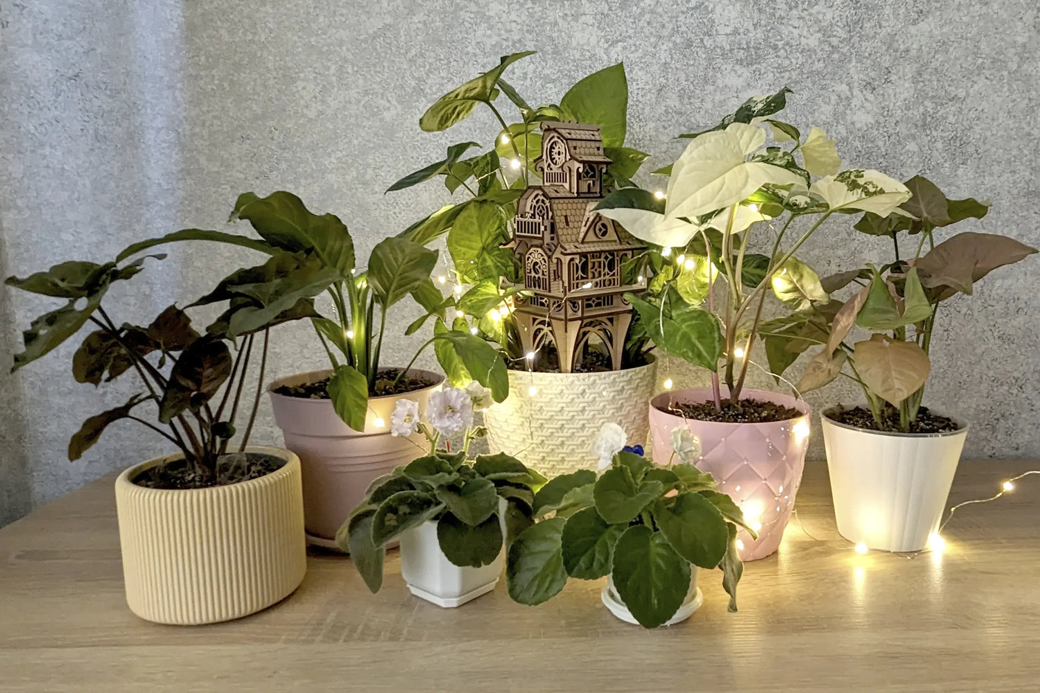 Laser cut plywood clock tower stakes inside a potted plant centerpiece, surrounded by home greenery and fairy lights.