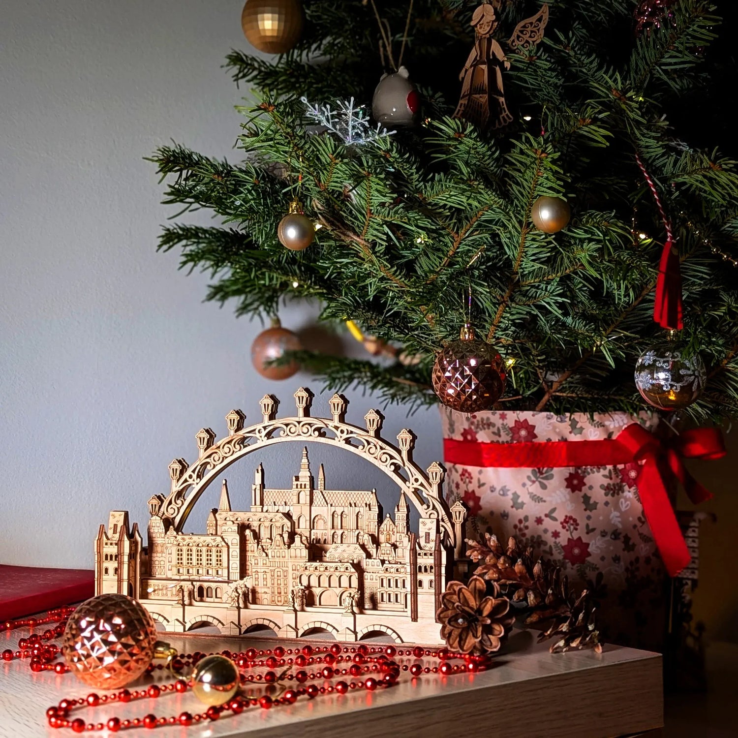 Ornate city skyline bridge crafted from laser cut plywood, styled under a decorated Christmas tree with red bead garland.