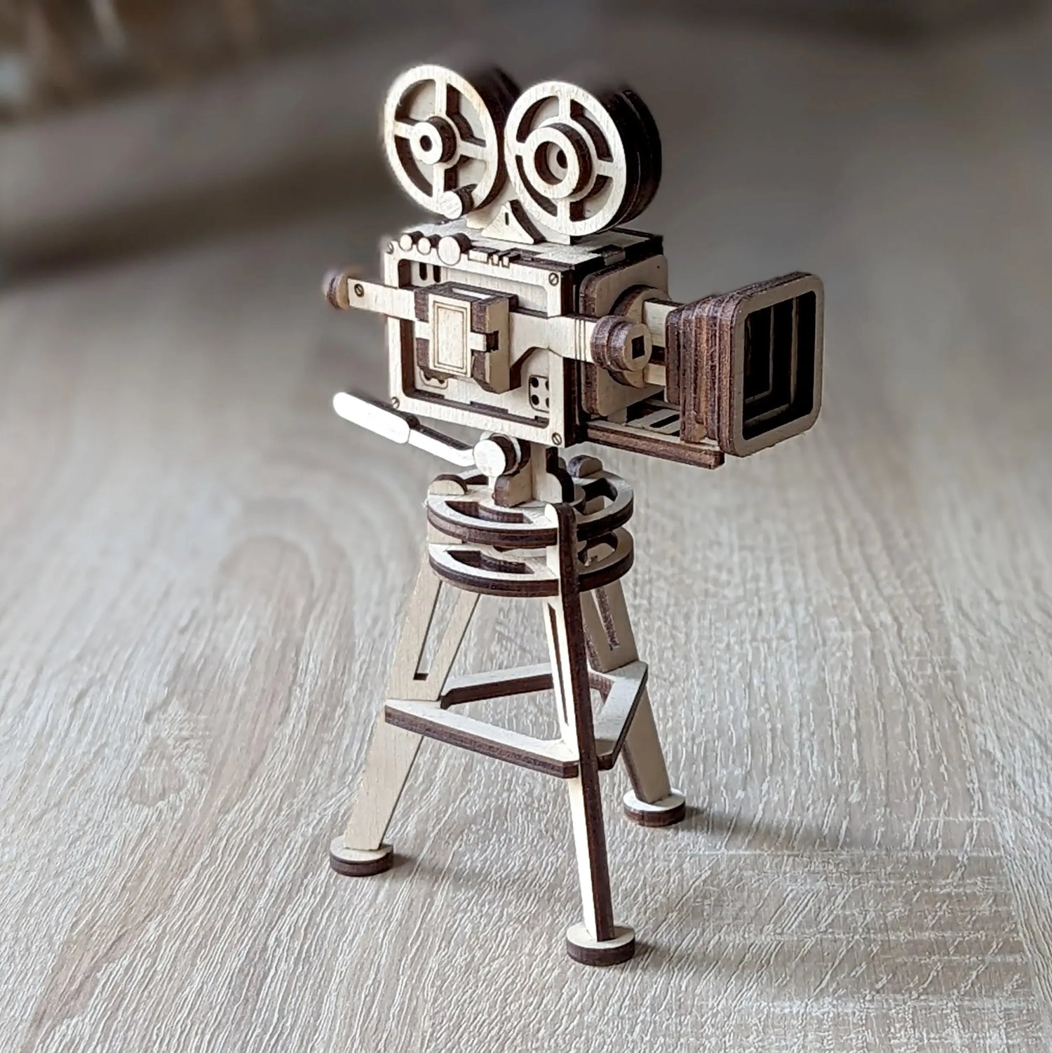 Vintage video camera model on a tripod, crafted from laser cut plywood with dark edges, standing on a light wooden table