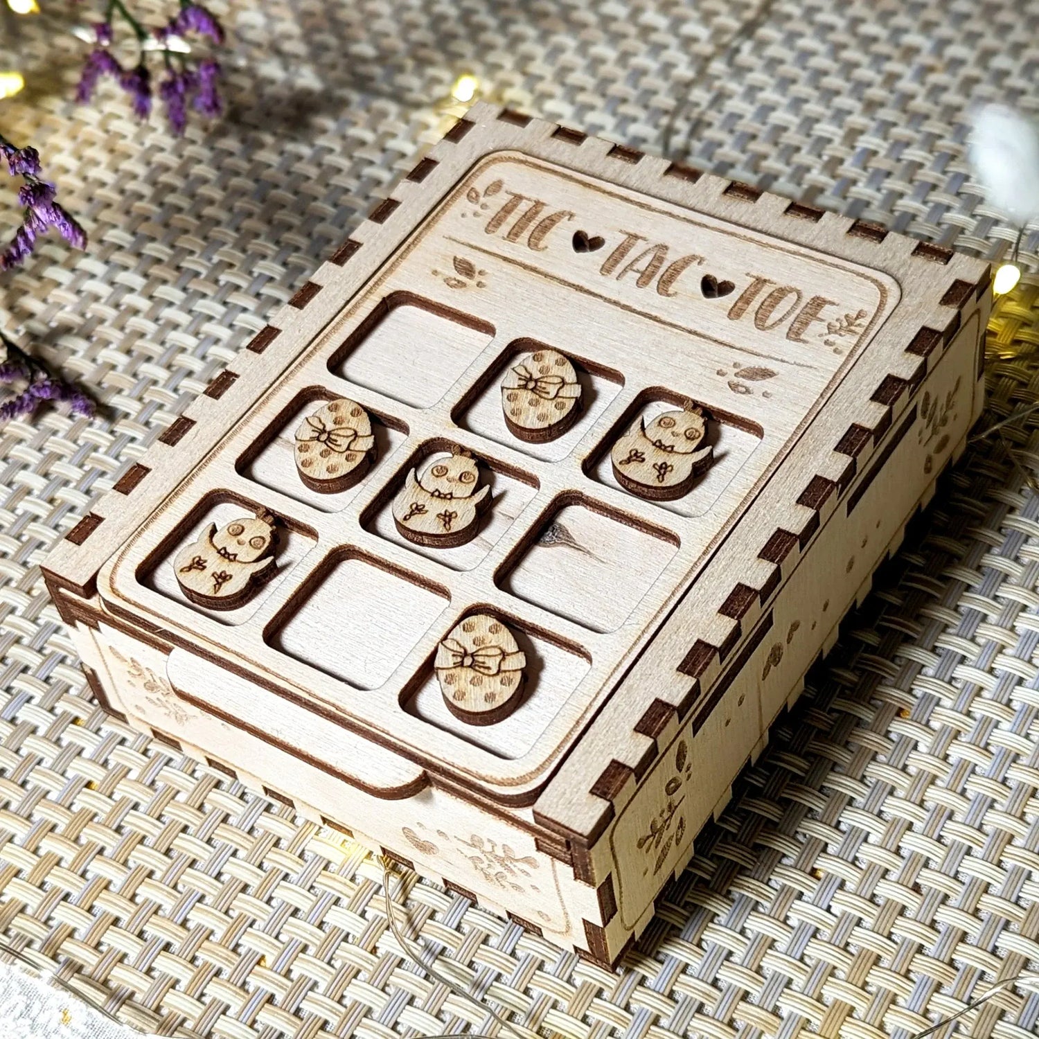 Easter tic-tac-toe game box made of laser cut plywood, featuring small engraved egg and chick tokens in the grid slots
