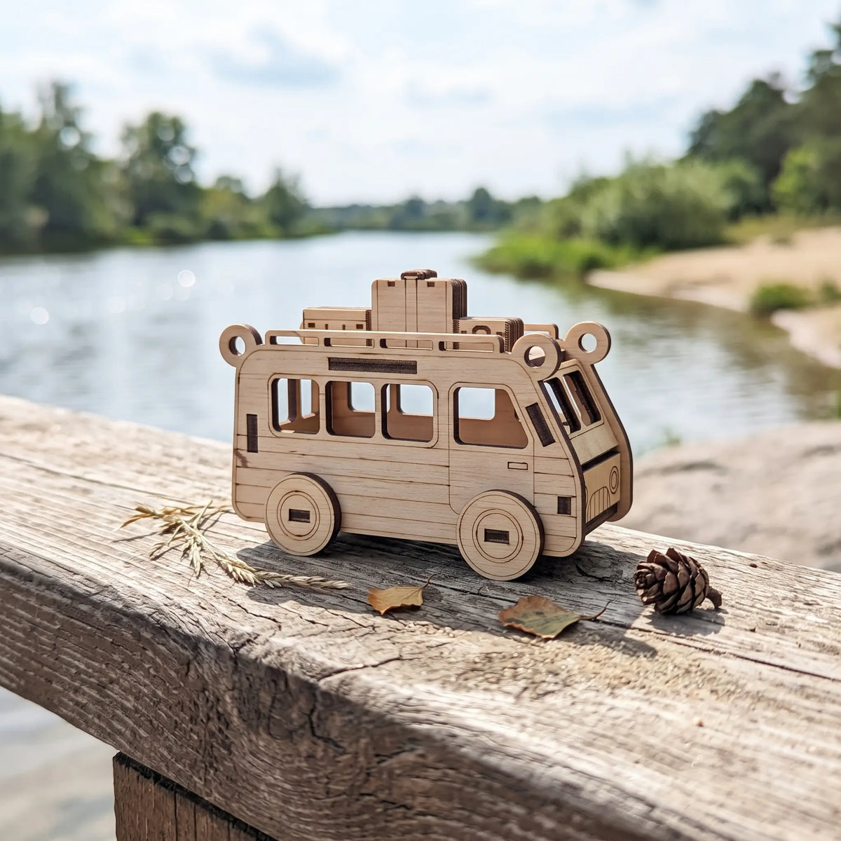 Natural laser cut plywood travel van figurine with roof luggage sitting on wooden bridge railing beside sunny river.