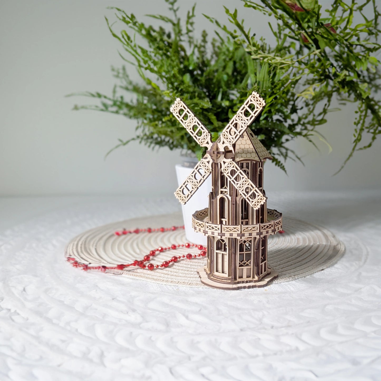 An assembled laser cut plywood Victorian windmill model displayed on a white table mat with a green plant background.