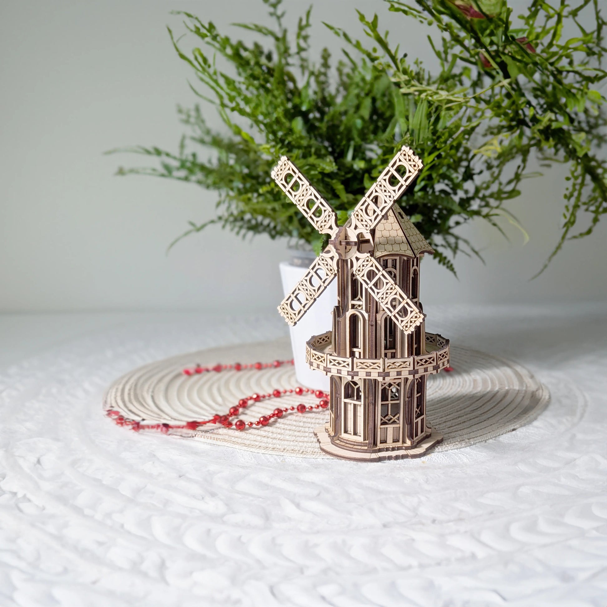 An assembled laser cut plywood Victorian windmill model displayed on a white table mat with a green plant background.