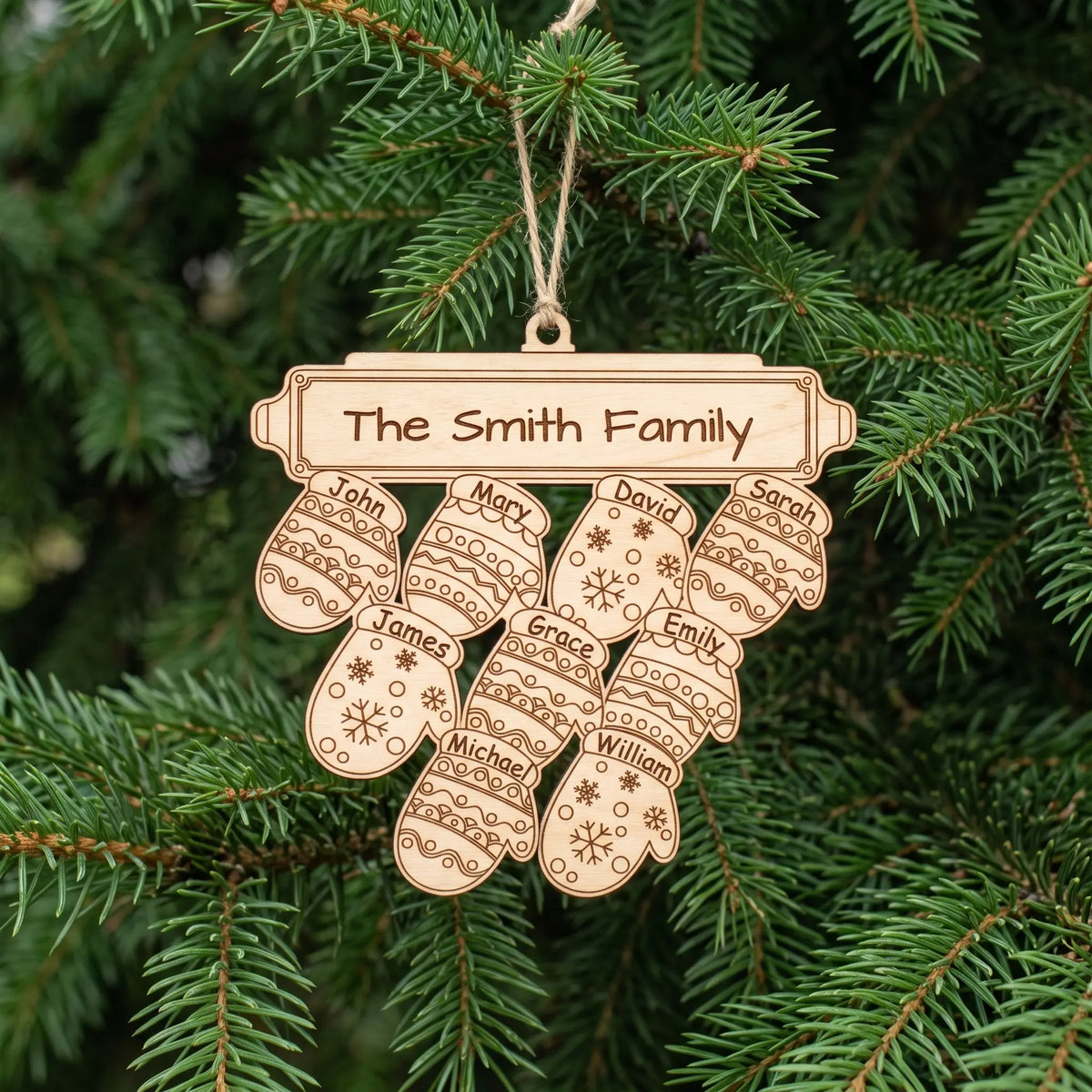 Natural laser cut plywood family mitten Christmas ornament with nine engraved names hanging by twine on green pine tree.