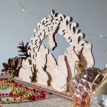 Side view of a laser cut wooden nativity scene with Mary, Joseph, baby Jesus, an angel, animals, and the three wise men under an ornate arch. Displayed with festive beads and pinecones