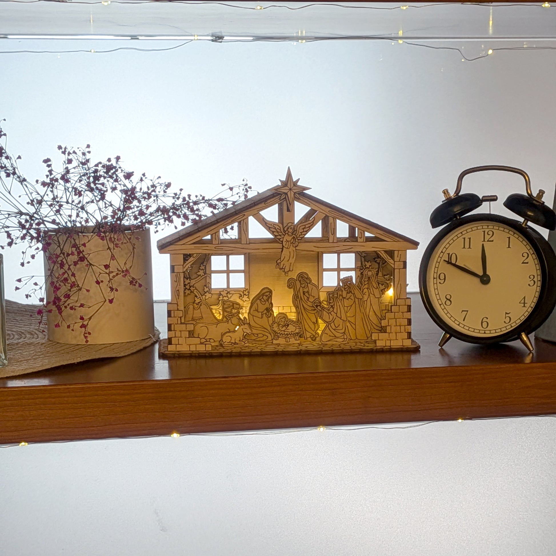 Wooden Nativity Scene displayed on a shelf with warm lights, featuring the Holy Family, shepherds, and animals. DIY Christmas decoration made from a laser cut digital file template