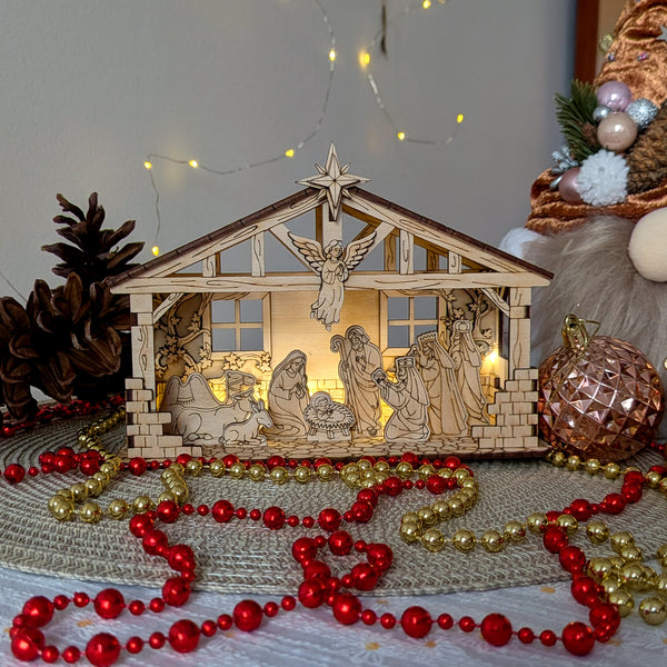 Wooden layered Nativity Scene with baby Jesus, Mary, Joseph, angel and the Three Wise Men inside a stable, displayed with Christmas ornaments and lights. Designed as a laser cut digital template for plywood