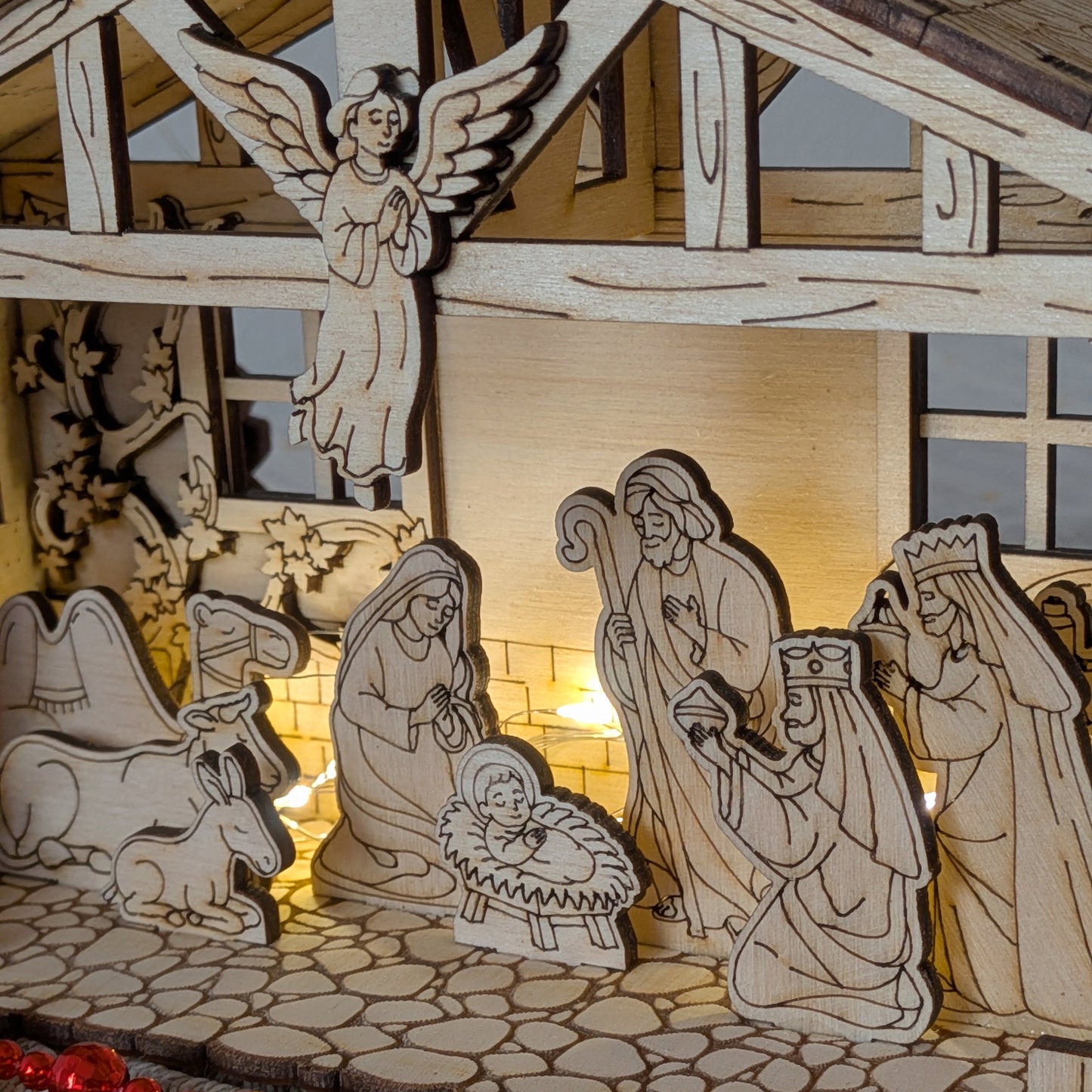 Close-up of a wooden Nativity Scene with the Holy Family, angel, animals, and Three Wise Men, illuminated with warm lights. DIY Christmas decor made from a laser cut digital template
