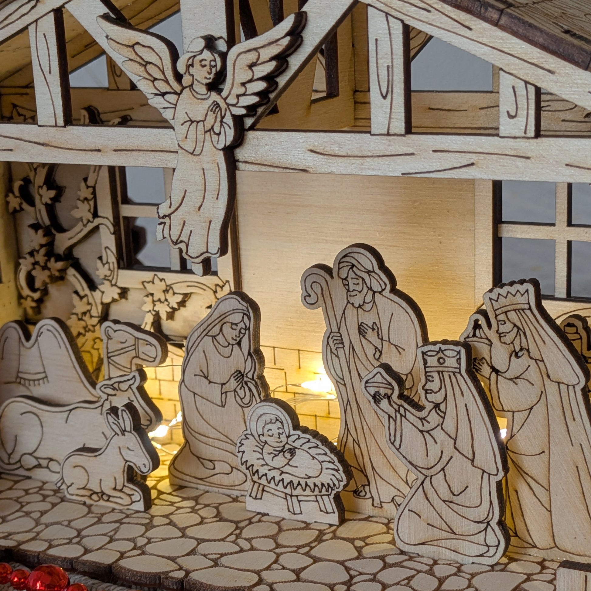 Close-up of a wooden Nativity Scene with the Holy Family, angel, animals, and Three Wise Men, illuminated with warm lights. DIY Christmas decor made from a laser cut digital template