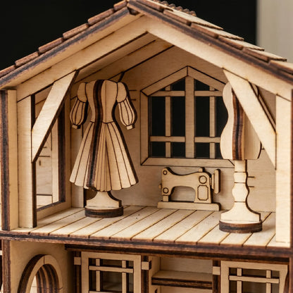 Wooden model of a house with a dress, sewing machine, and lamp inside