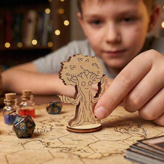 A close-up view of a laser-cut plywood forest mage miniature being played on a hexagonal tabletop game map. A hand moves the sentient tree character among RPG accessories, including a d20 die and small potion jars, during a gaming session.
