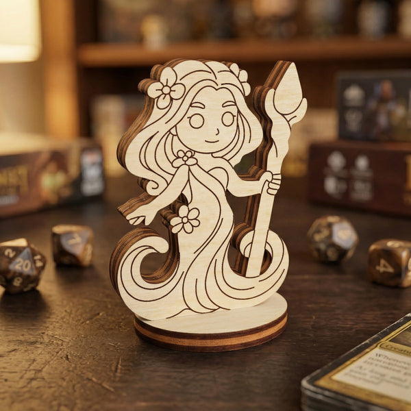 A close-up of a handcrafted forest dryad miniature made from layered laser-cut wood. The design emphasizes a cute, fantasy-themed character with floral accents. Posed on a wooden surface with blurred gaming dice and card boxes in the background, highlighting its use as a tabletop accessory.