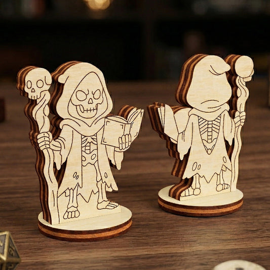Front and back views of a 3D laser-cut plywood Dark Necromancer figurine. The skeletal character wears a hooded, tattered robe and holds a skull-topped staff and an open spellbook. Displayed on a wooden tabletop with polyhedral gaming dice in a cozy fantasy setting.