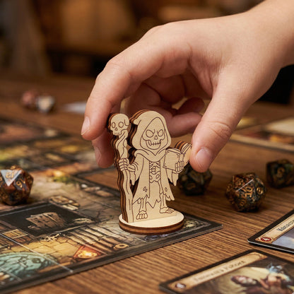 An action shot of a person's hand placing a wooden laser-cut necromancer figurine on a dungeon-themed tabletop game board. Surrounded by polyhedral dice and gaming cards, highlighting the figurine's scale and use in a roleplaying game.