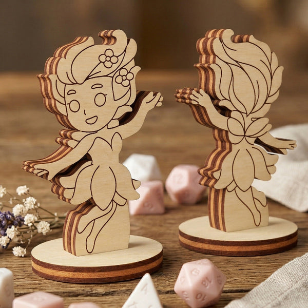 Front and back view of a blossom fairy figurine made of laser cut plywood on a wooden table with gaming dice and lavender.