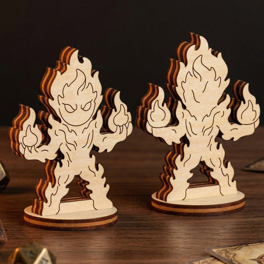 Front and back views of a fire elemental figurine made of laser cut plywood, surrounded by metal D&D dice and fantasy cards.