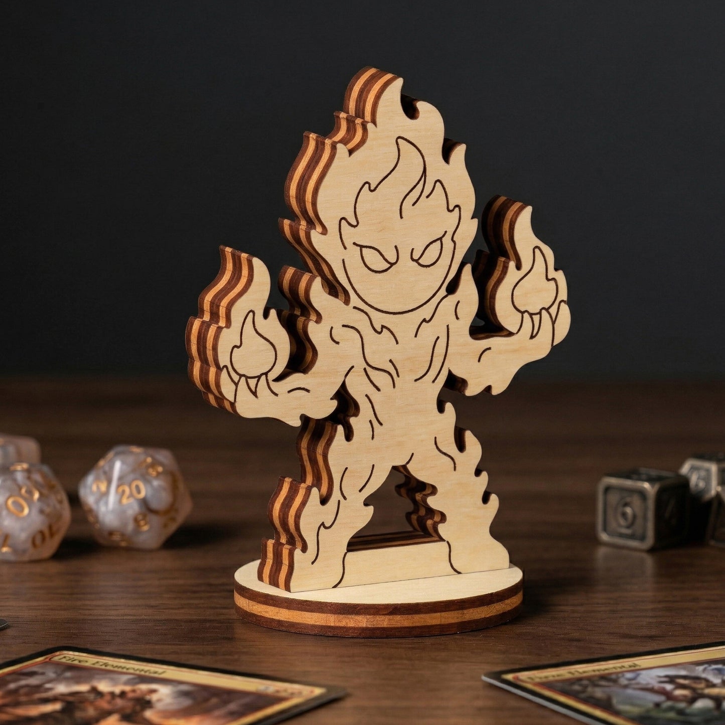 Detailed view of a laser cut plywood fire elemental figurine with engraved flames, standing on a table with RPG dice and cards.