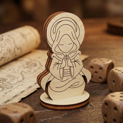 Close-up of a laser cut plywood holy monk figurine with detailed engravings of a hooded figure praying among wooden dice.