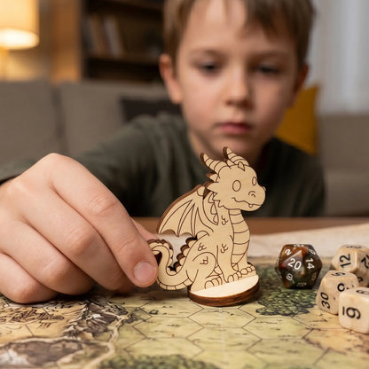 A child’s hand holds a laser cut plywood dragon miniature on a hex grid game map. Scale is shown next to standard gaming dice.