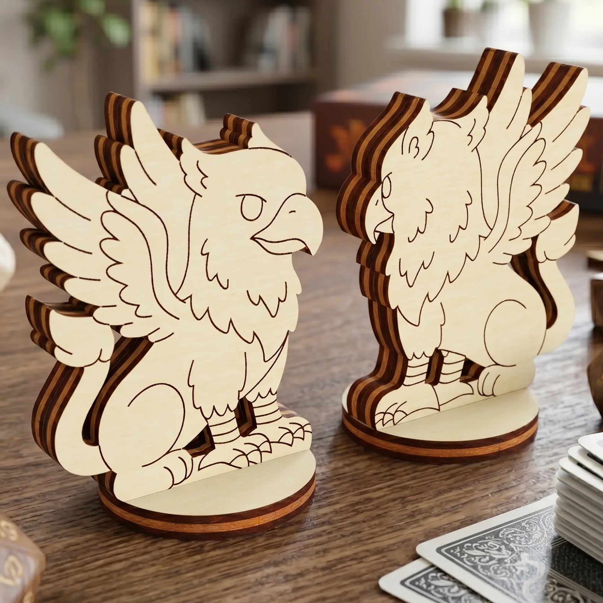 Front and back view of two griffin figurines made of laser cut plywood, standing on a table with RPG dice and gaming cards.