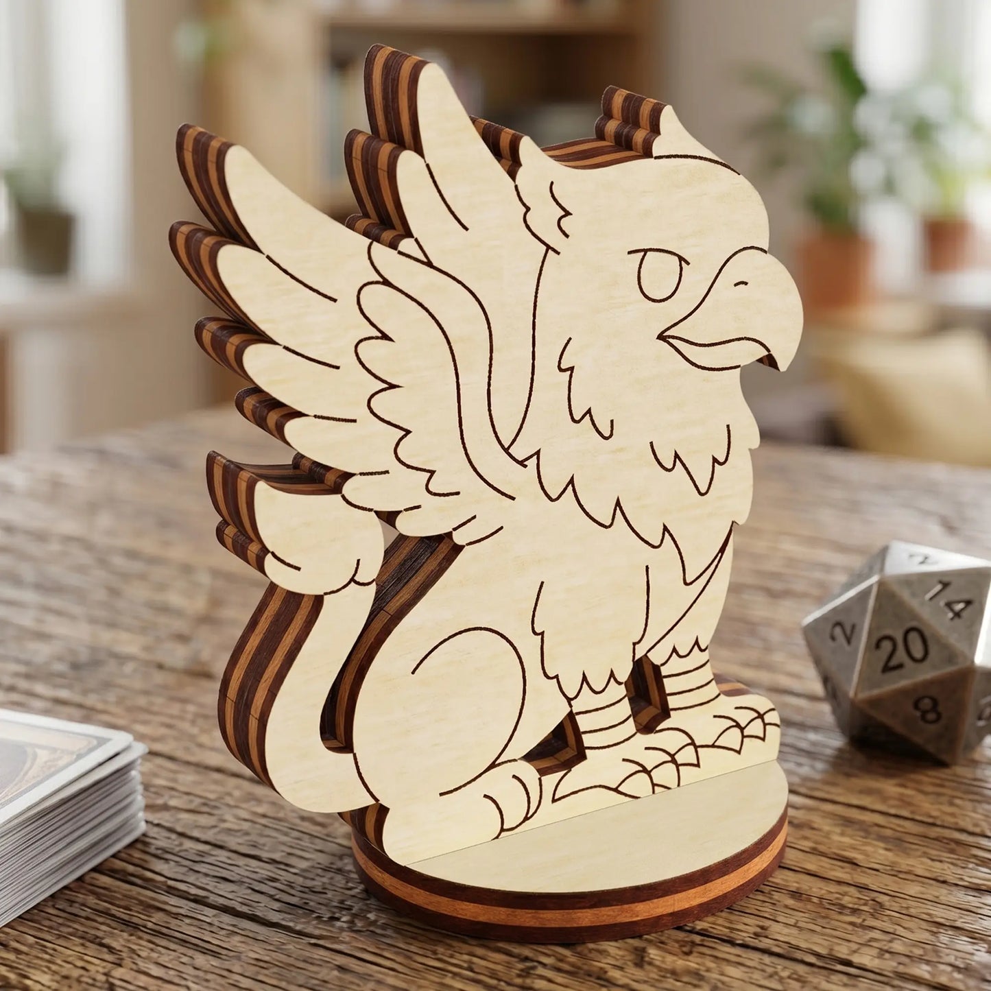Close-up of a laser cut plywood griffin figurine with engraved wings and feathers, standing next to a metal twenty-sided die.