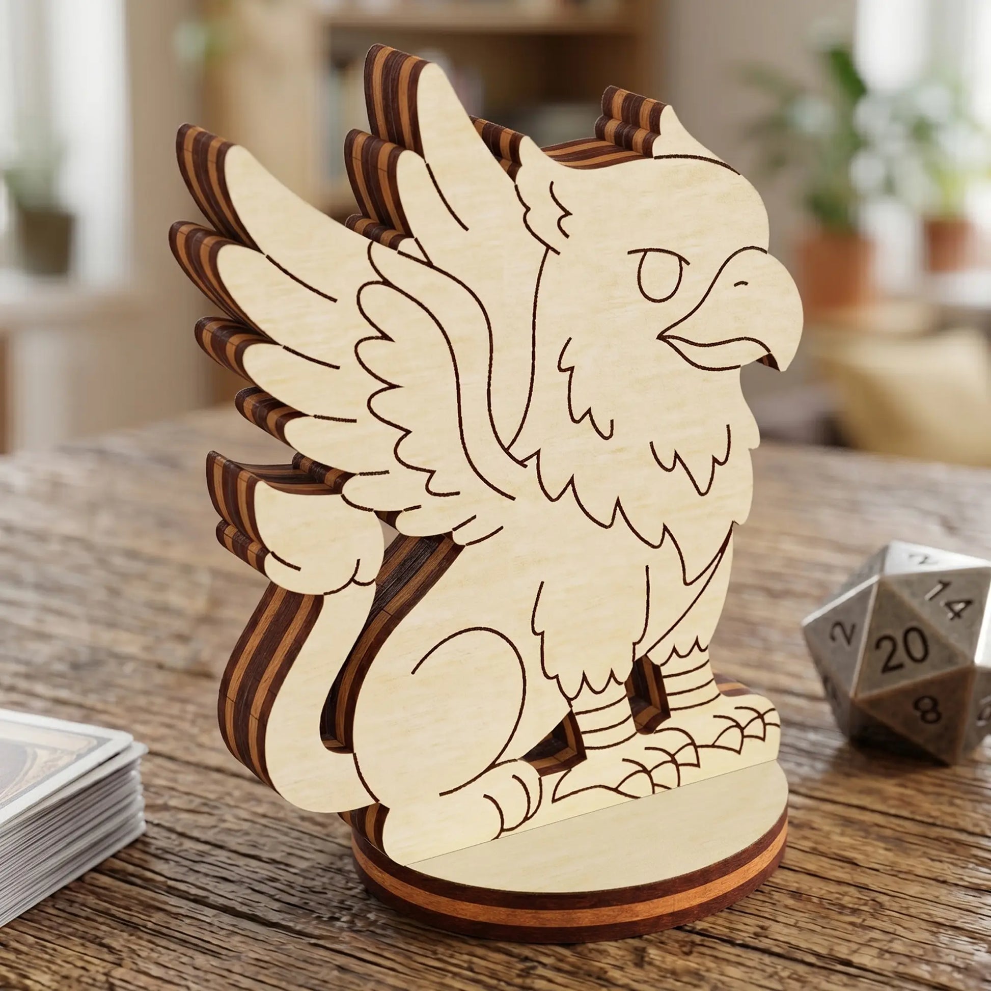Close-up of a laser cut plywood griffin figurine with engraved wings and feathers, standing next to a metal twenty-sided die.