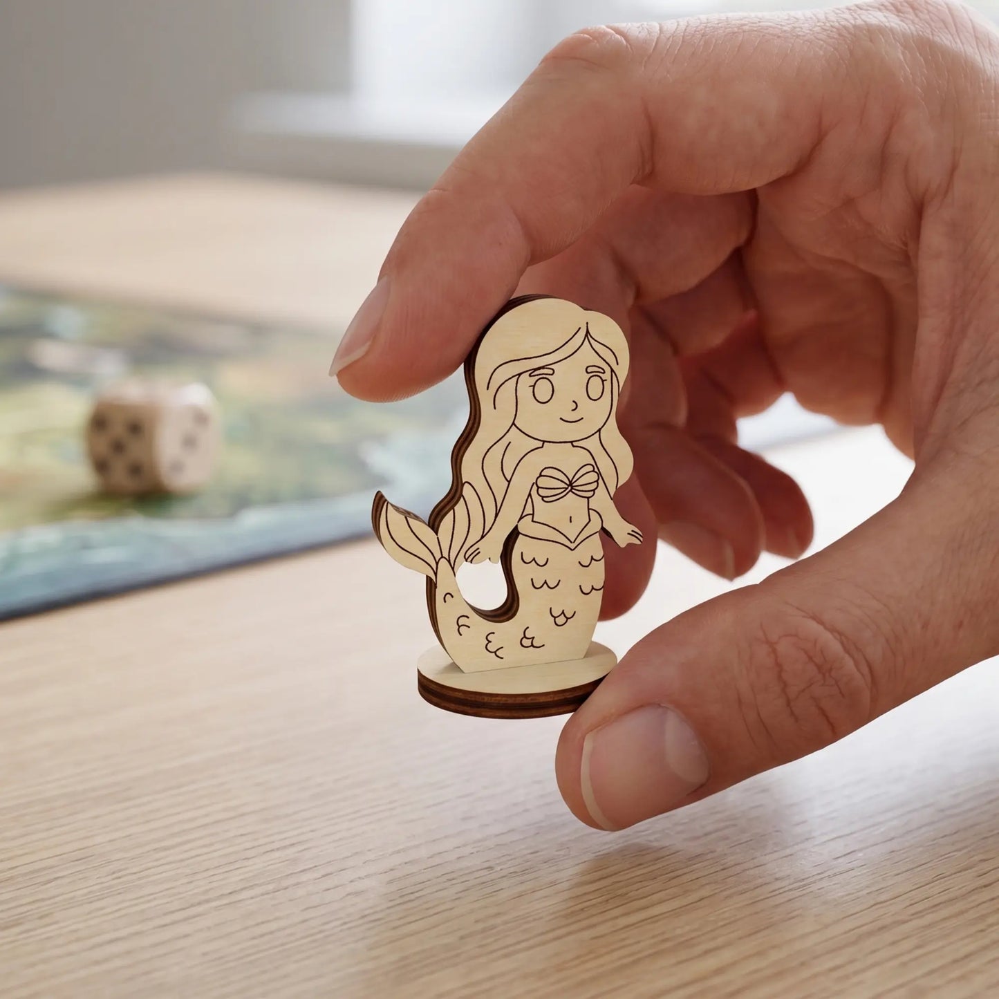 Adult hand holding a tiny laser cut plywood mermaid figurine between fingers to show the true miniature tabletop scale.