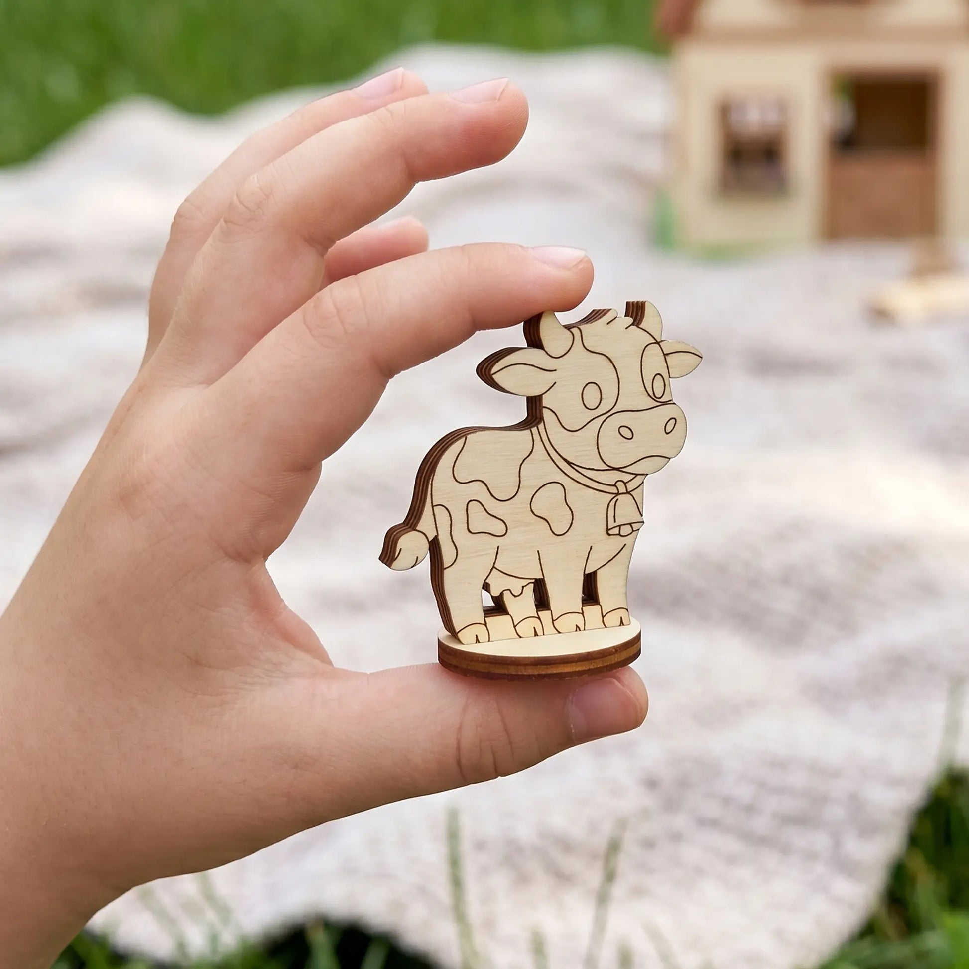 Tiny cow figurine made of laser cut plywood held in a child's hand to demonstrate its miniature scale.