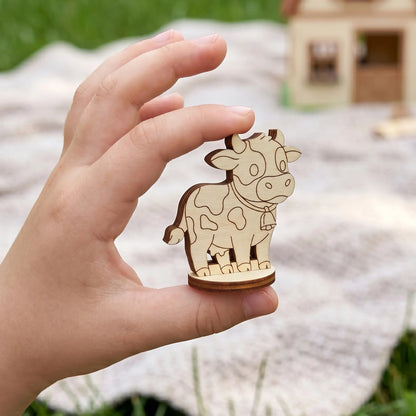Tiny cow figurine made of laser cut plywood held in a child's hand to demonstrate its miniature scale.