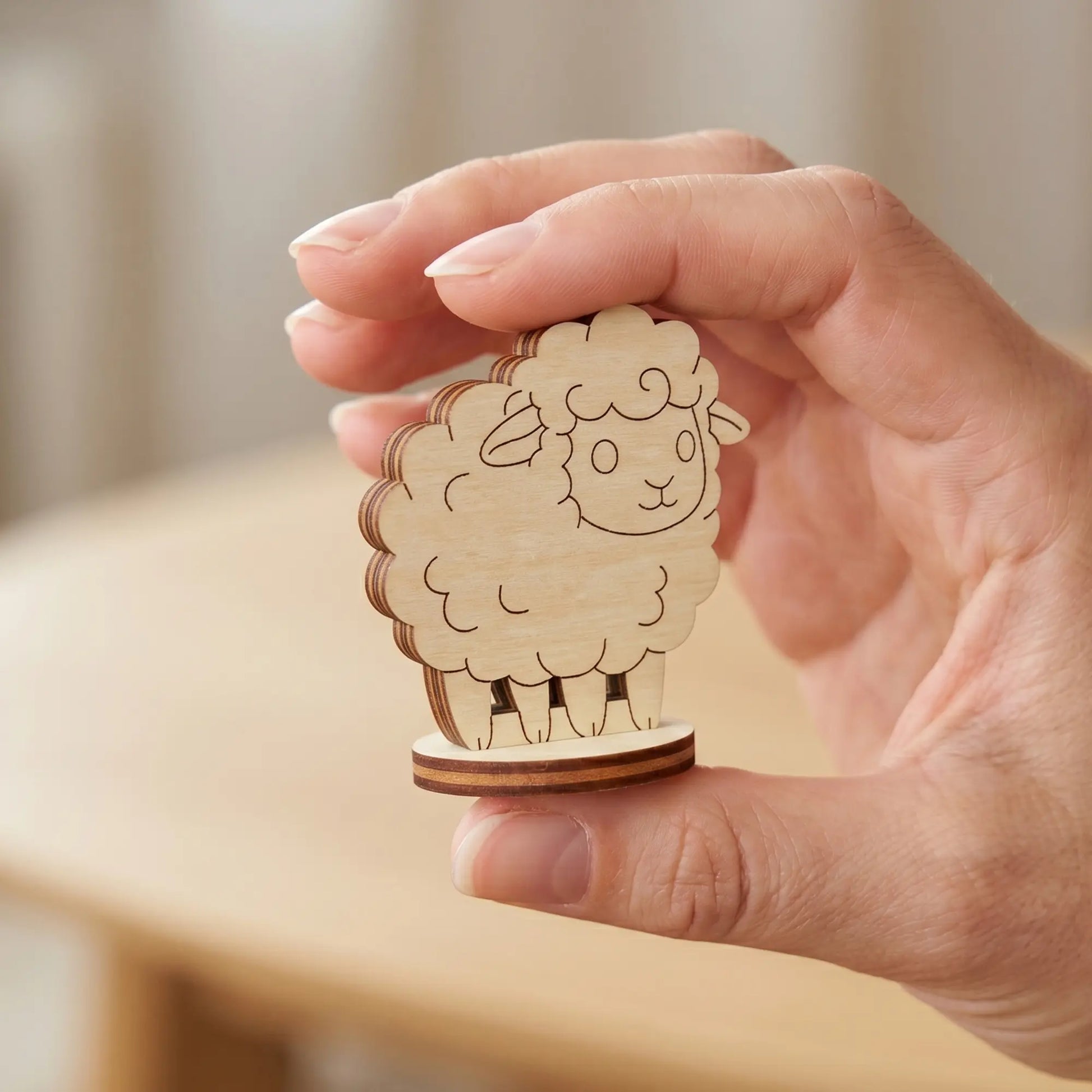 Tiny sheep figurine made of laser cut plywood held between fingers to showcase its small miniature scale.