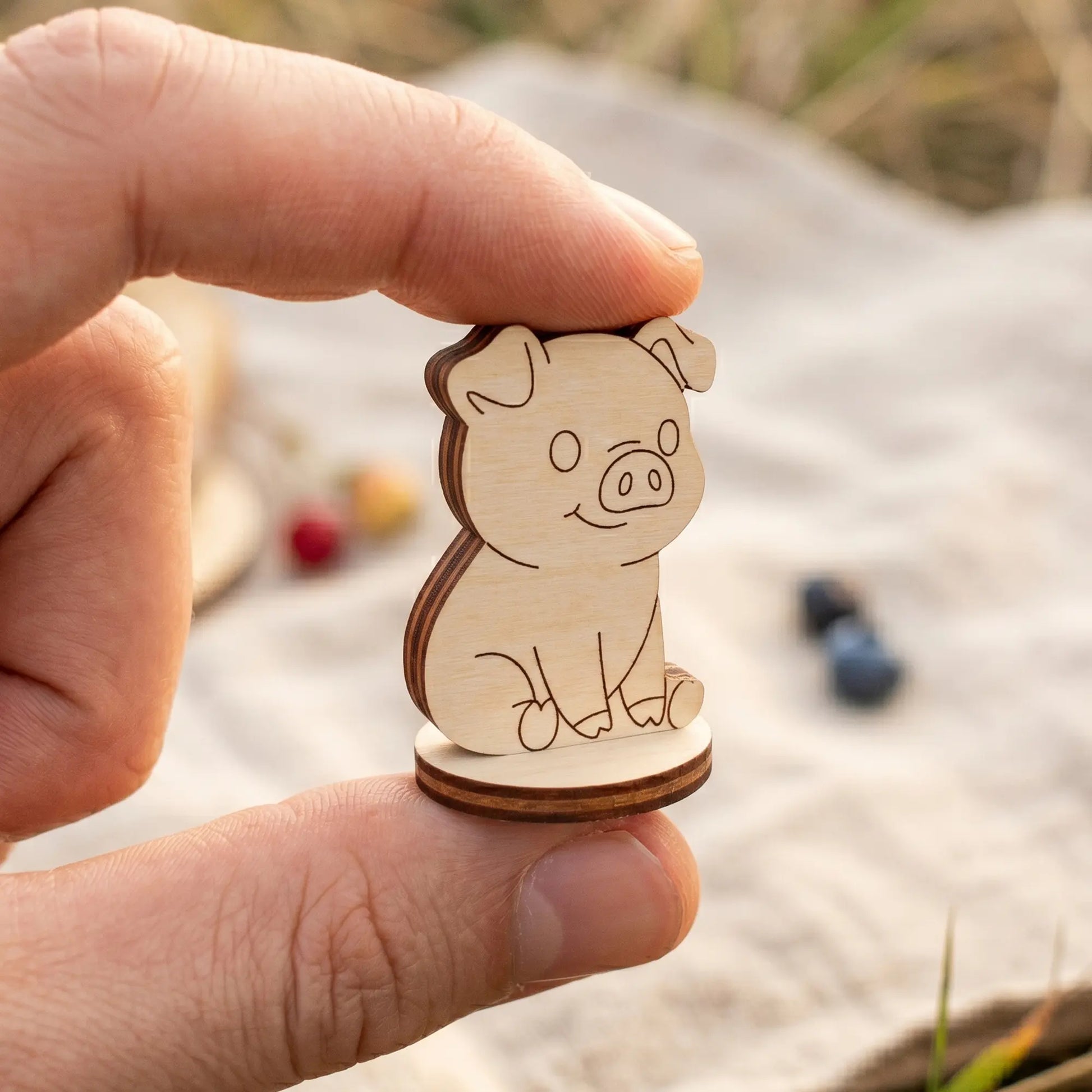 Close-up showing a person's fingers holding a tiny runic scale pig token made of premium laser cut plywood wood.