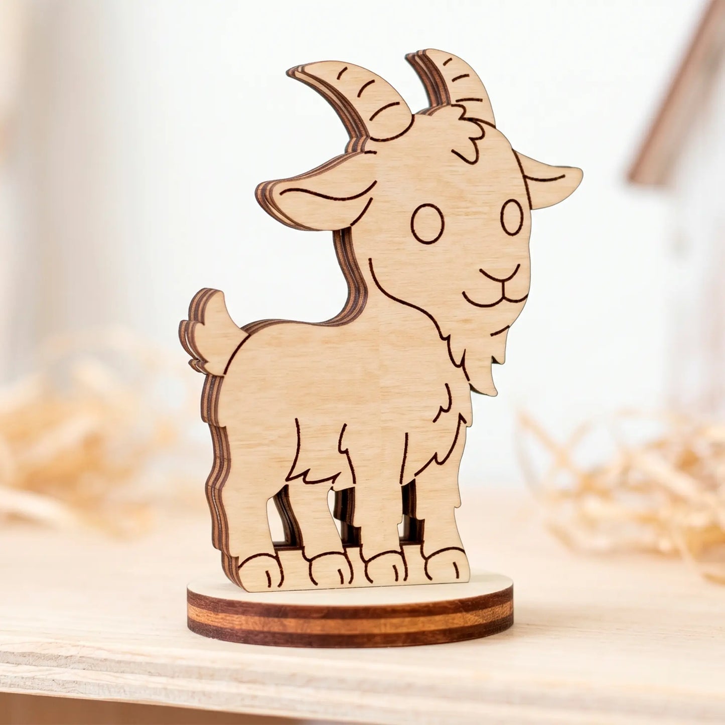 Close-up of an unpainted miniature laser cut plywood goat figurine standing on a light wooden table surface.
