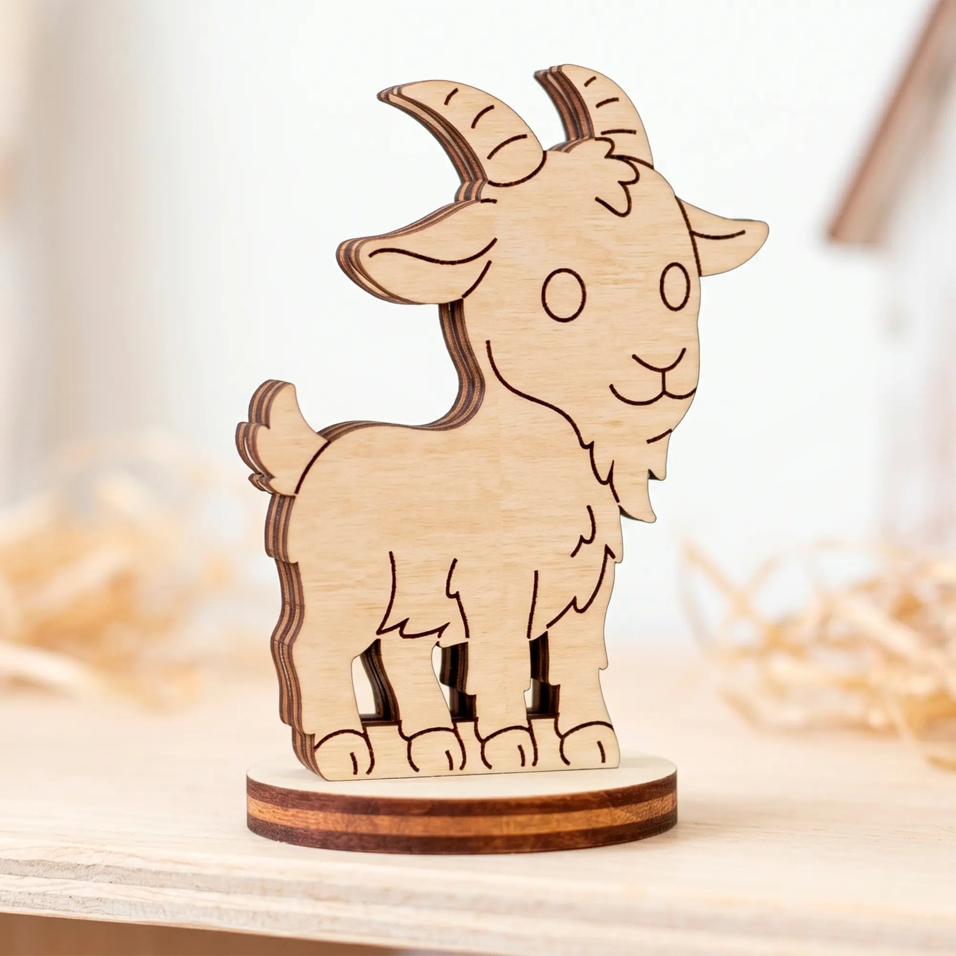 Close-up of an unpainted miniature laser cut plywood goat figurine standing on a light wooden table surface.