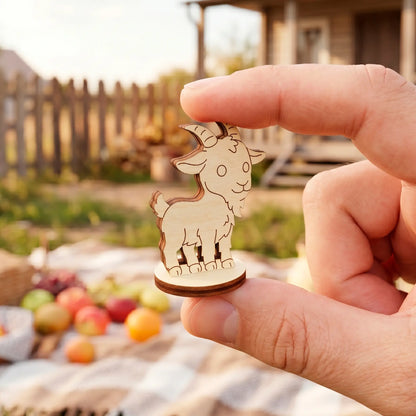 Close-up showing fingers holding a miniature standing goat figurine made of laser cut plywood over a picnic setup.