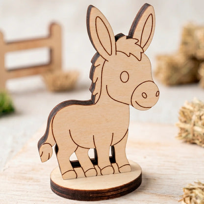 Close-up of an unpainted miniature laser cut plywood donkey figurine standing on a light wooden table surface.
