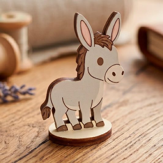 A hand-painted grey miniature donkey figurine with details, made of laser cut plywood on a wooden workshop table.