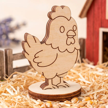 Laser cut plywood cute hen miniature on a straw bedding with grain near a blurred red toy farmhouse and wooden fence