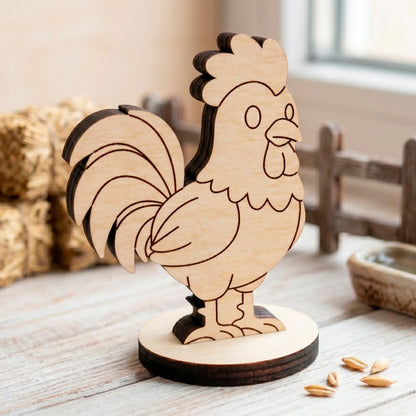 Laser cut plywood cute rooster miniature on a light surface with wheat grains near a small fence and blurred hay bales.